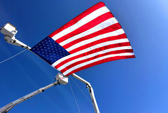 A large American flag is suspended in the air between two elevated work platforms against a clear blue sky. Description generated by AI